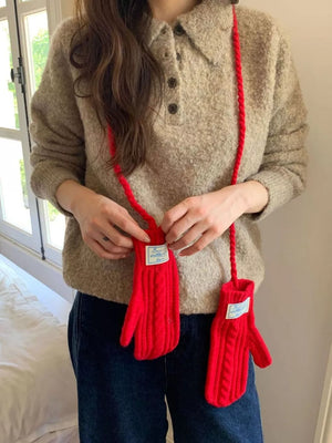 Red cable knit acrylic gloves with white labels, worn as a crossbody accessory.