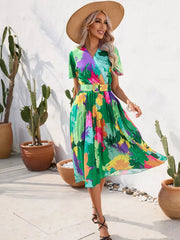 Tropical pleated midi dress with belt in vibrant floral print, featuring a wrap neckline and short sleeves.