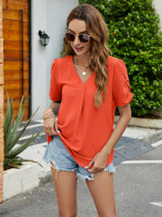 Textured orange blouse with V-neck, pleats, and ruched sleeves.
