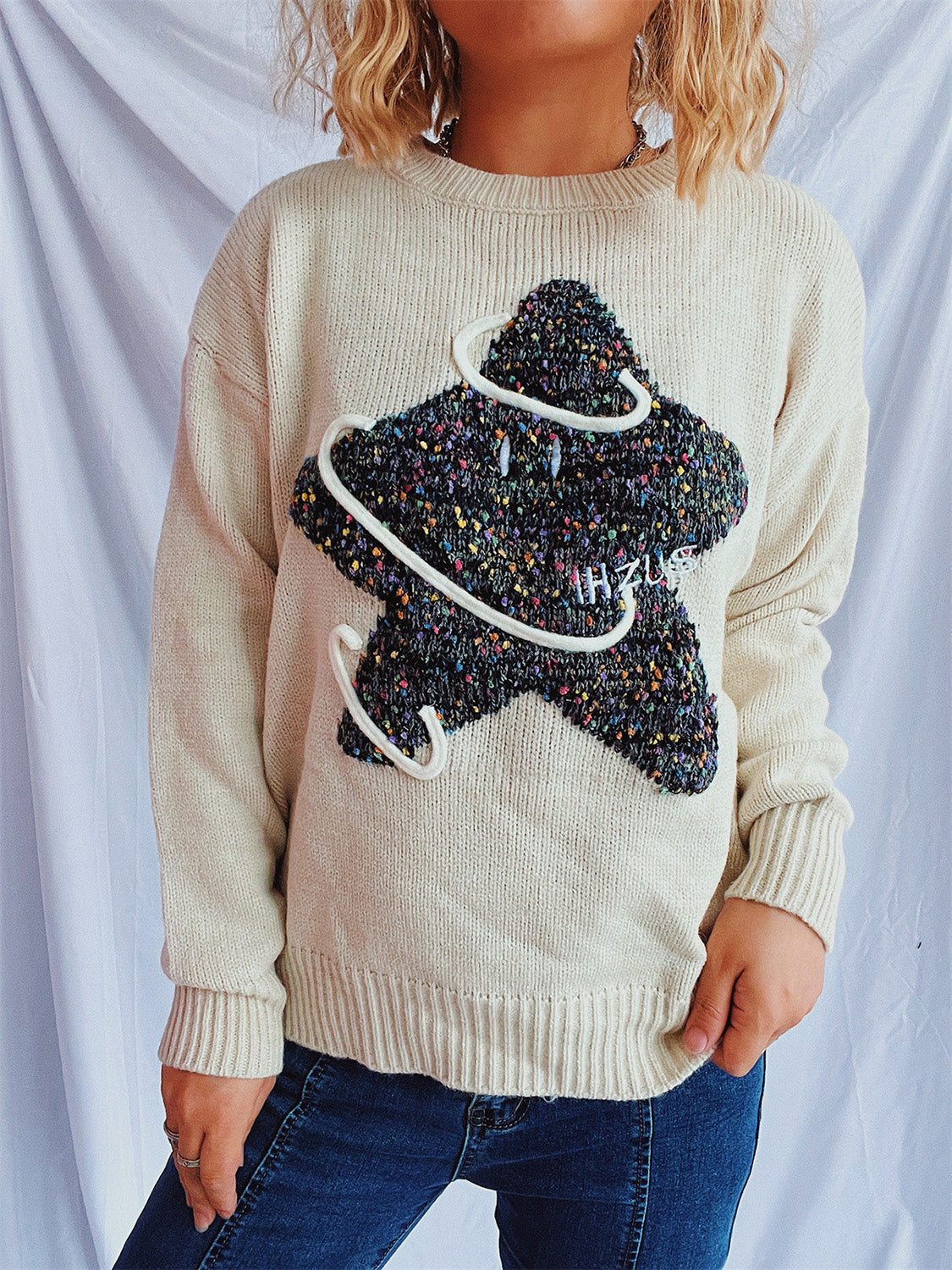 Beige knit jumper with embroidered starburst detail and white piping.