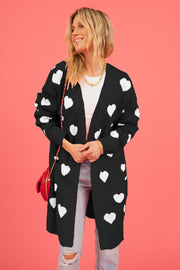 Black longline knit cardigan with white heart motif, pockets, and open front.
