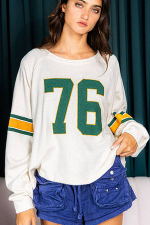White raglan sleeve sweatshirt with green and yellow '76' graphic and striped sleeves.