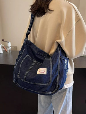 Slouchy dark blue denim crossbody bag with contrast stitching and distressed details.