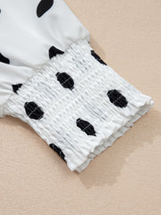 White polka dot blouse with smocked cuffs and ruffled hem detail.