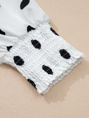 White polka dot blouse with smocked cuffs and ruffled hem detail.