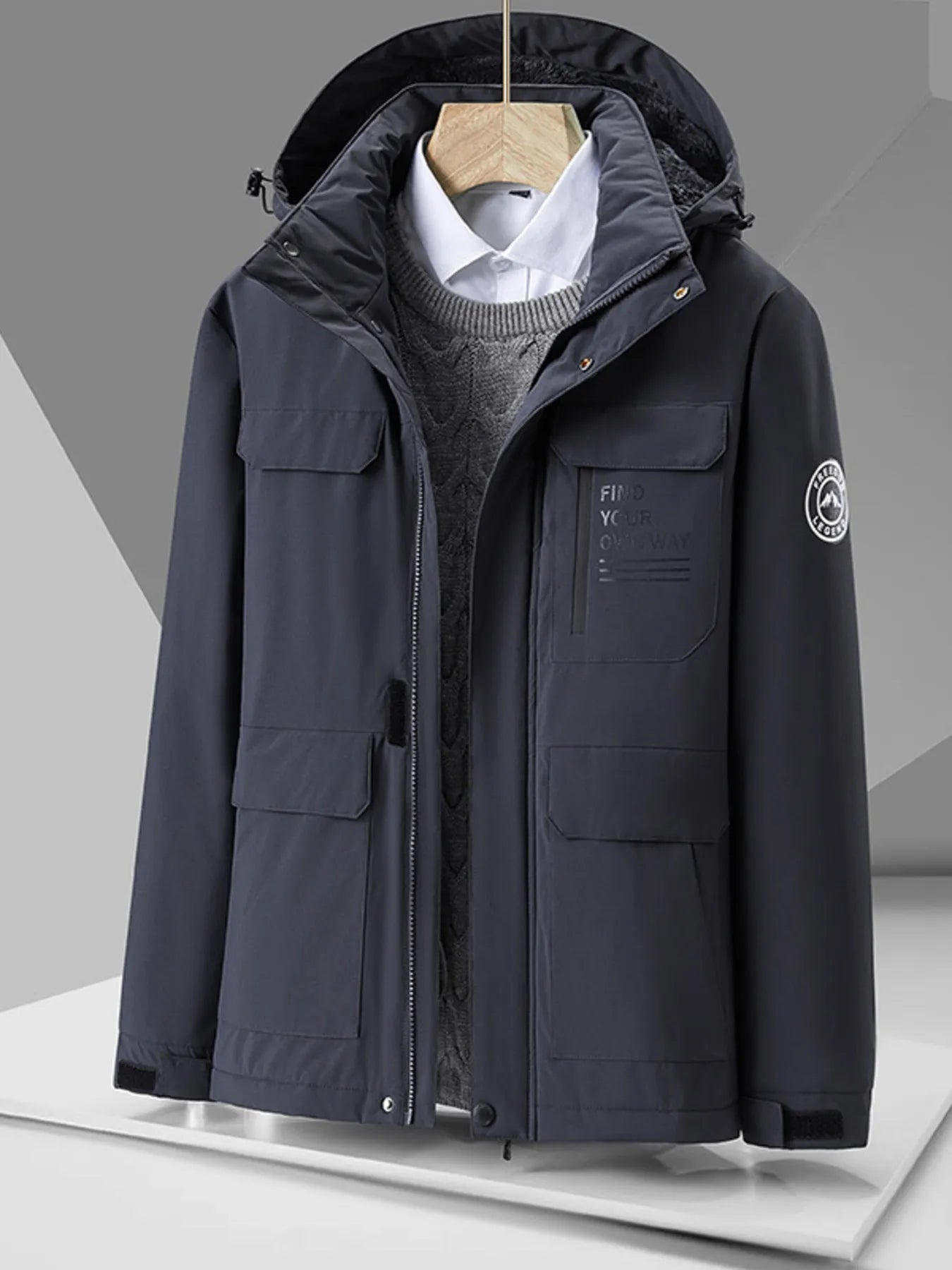 Dark grey hooded puffer jacket with multiple pockets and embroidered text detail.