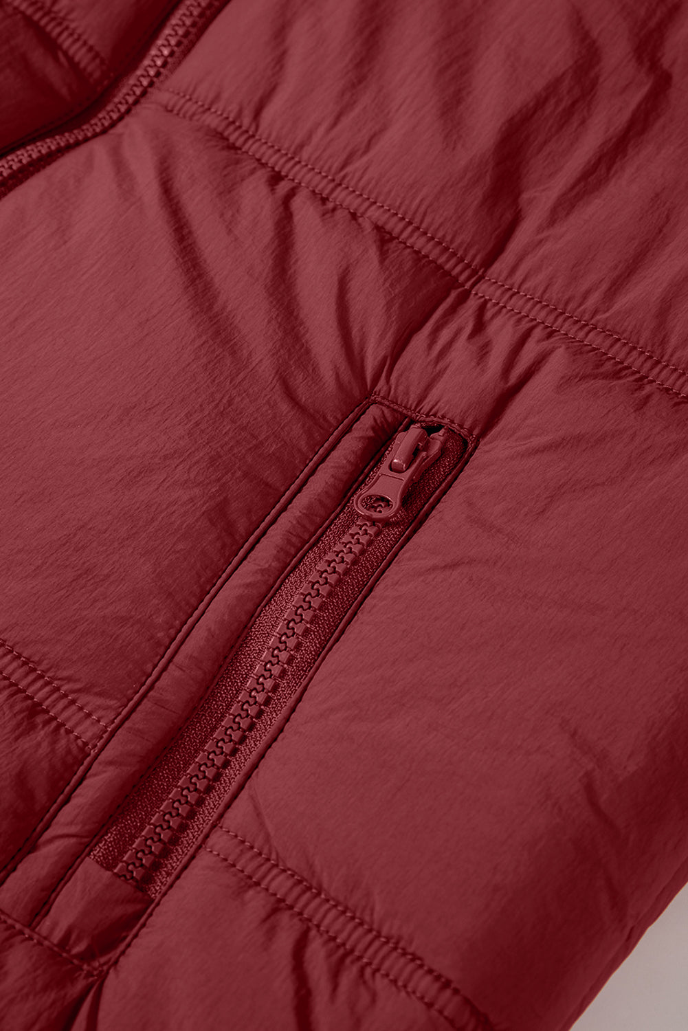 Burgundy quilted puffer vest detail showing a zippered pocket and stitching.