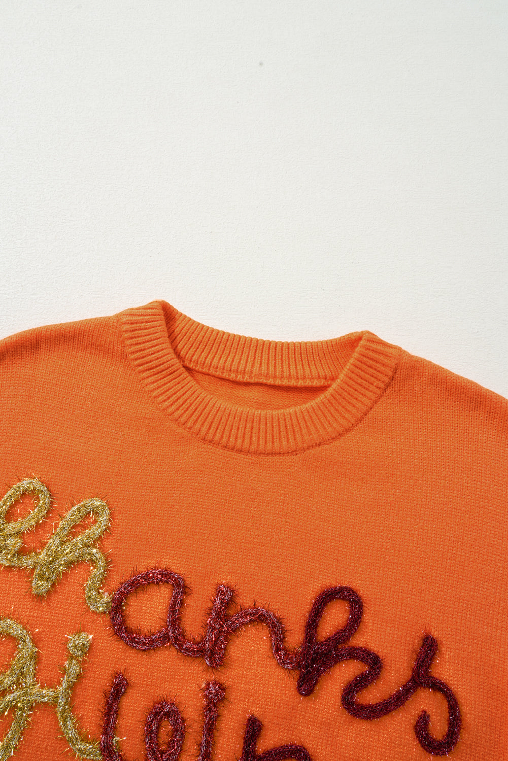 Orange knit sweater with sequin script detail and crew neck.
