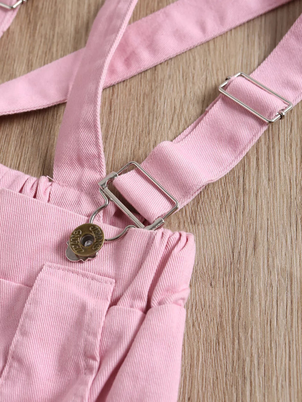 Pink denim baby overalls with adjustable straps and silver hardware detail.