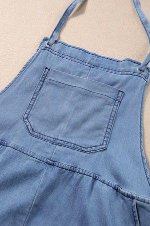 Medium wash denim romper with adjustable straps and a large front bib pocket.