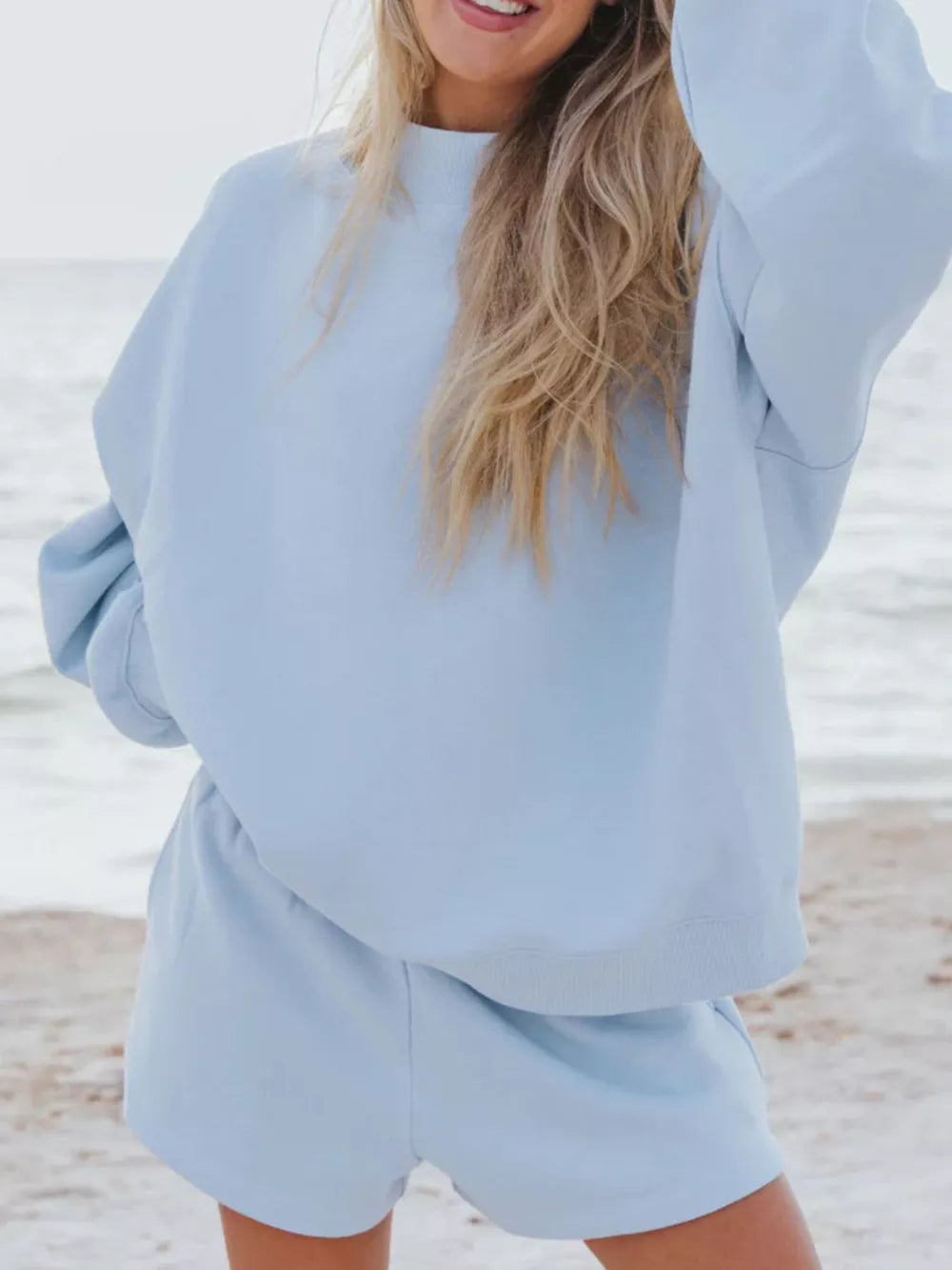 Sky blue crew neck sweatshirt and shorts lounge set on a beach.