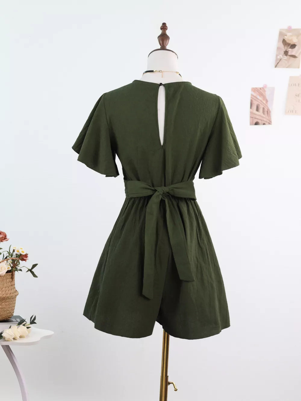Olive green romper with flutter sleeves, tie waist, and keyhole back detail.