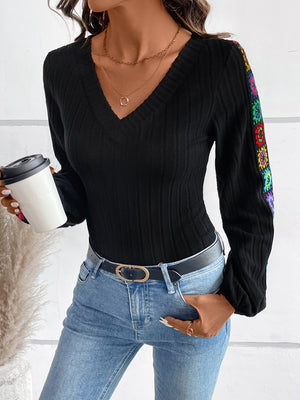 Black ribbed knit v-neck blouse with colorful embroidered sleeves.