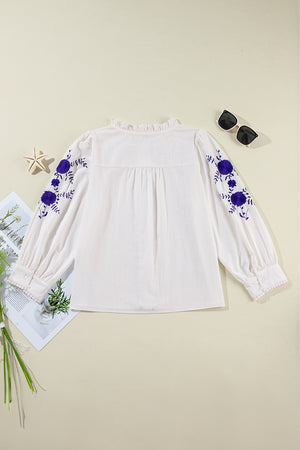 White embroidered blouse with ruffled neckline, long sleeves, and scalloped trim.