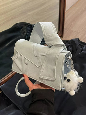 Artisanal mini denim crossbody bag in light blue with a fluffy keychain detail.