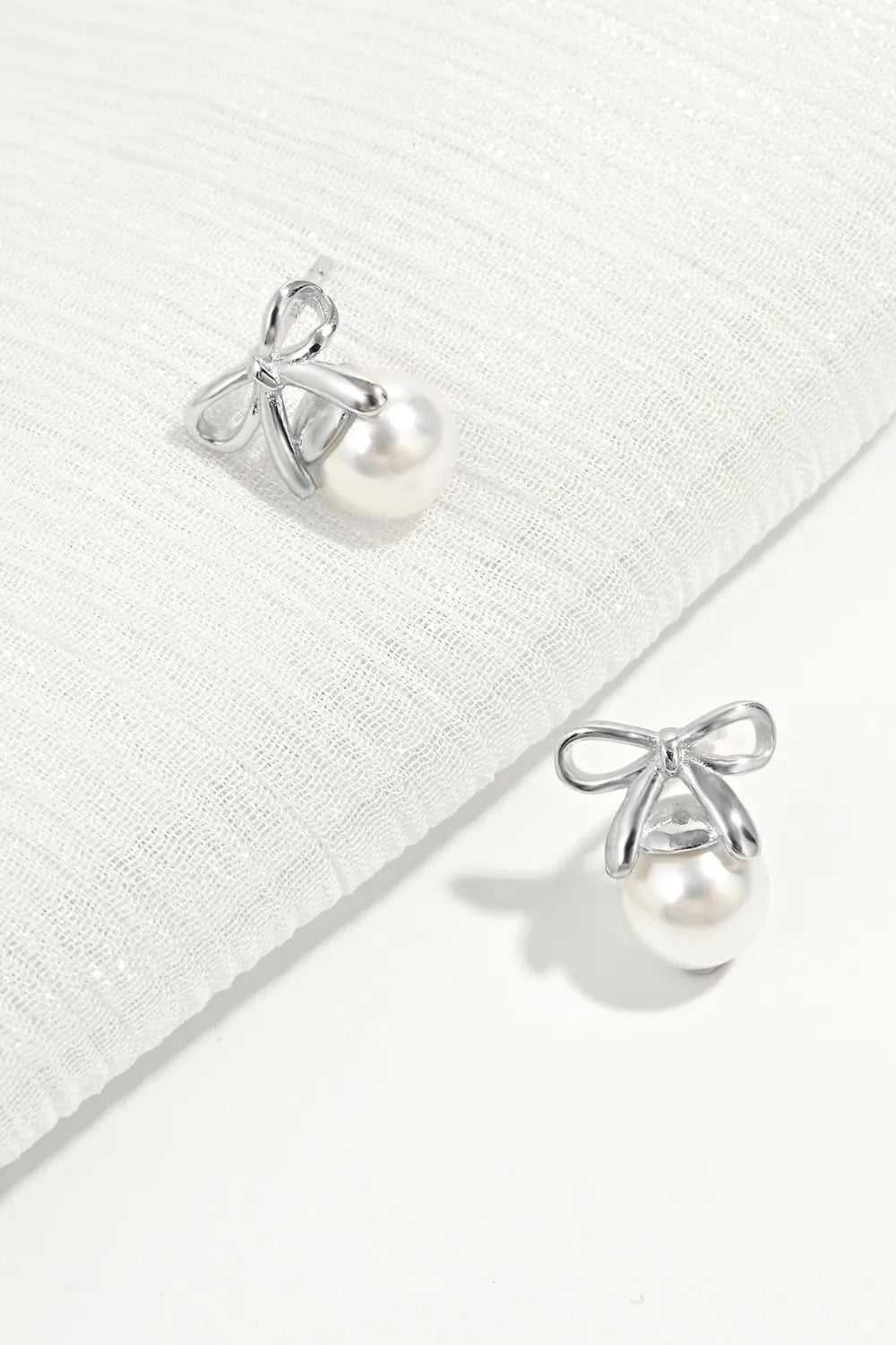 Silver bow pearl drop earrings with a classic pearl and delicate bow detail.
