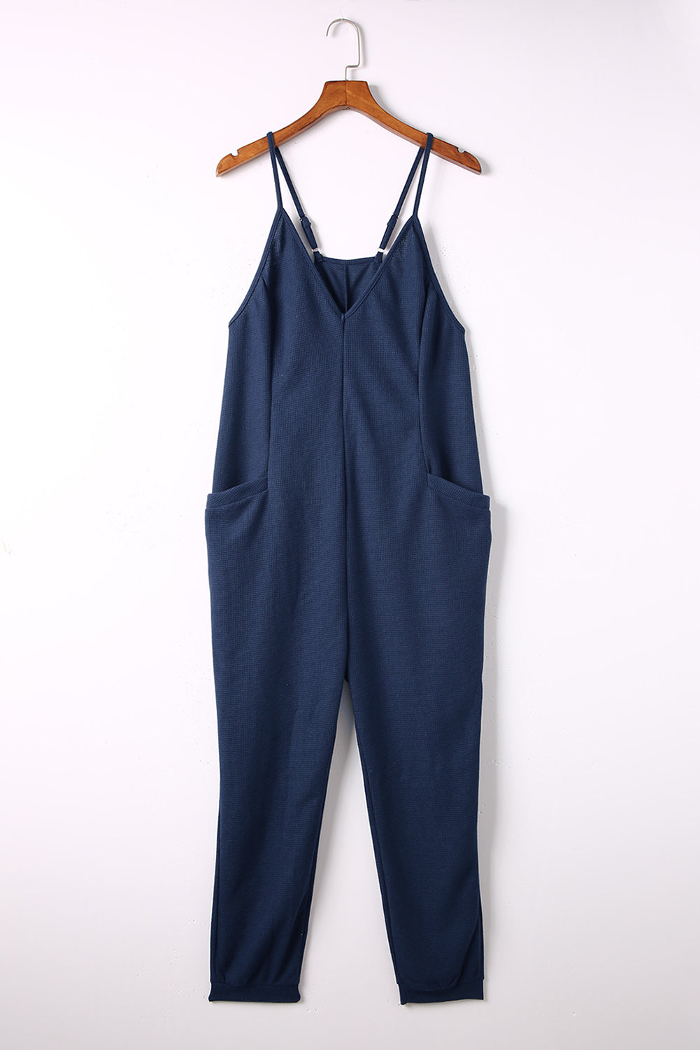 Navy jersey jumpsuit with V-neck, spaghetti straps, and slouch pockets.