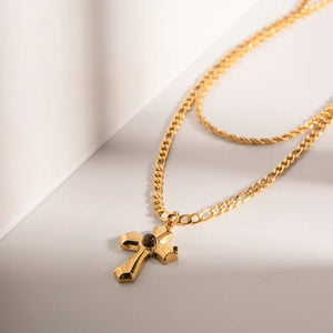Gold layered chain necklace with a sculpted cross pendant featuring a dark stone accent.