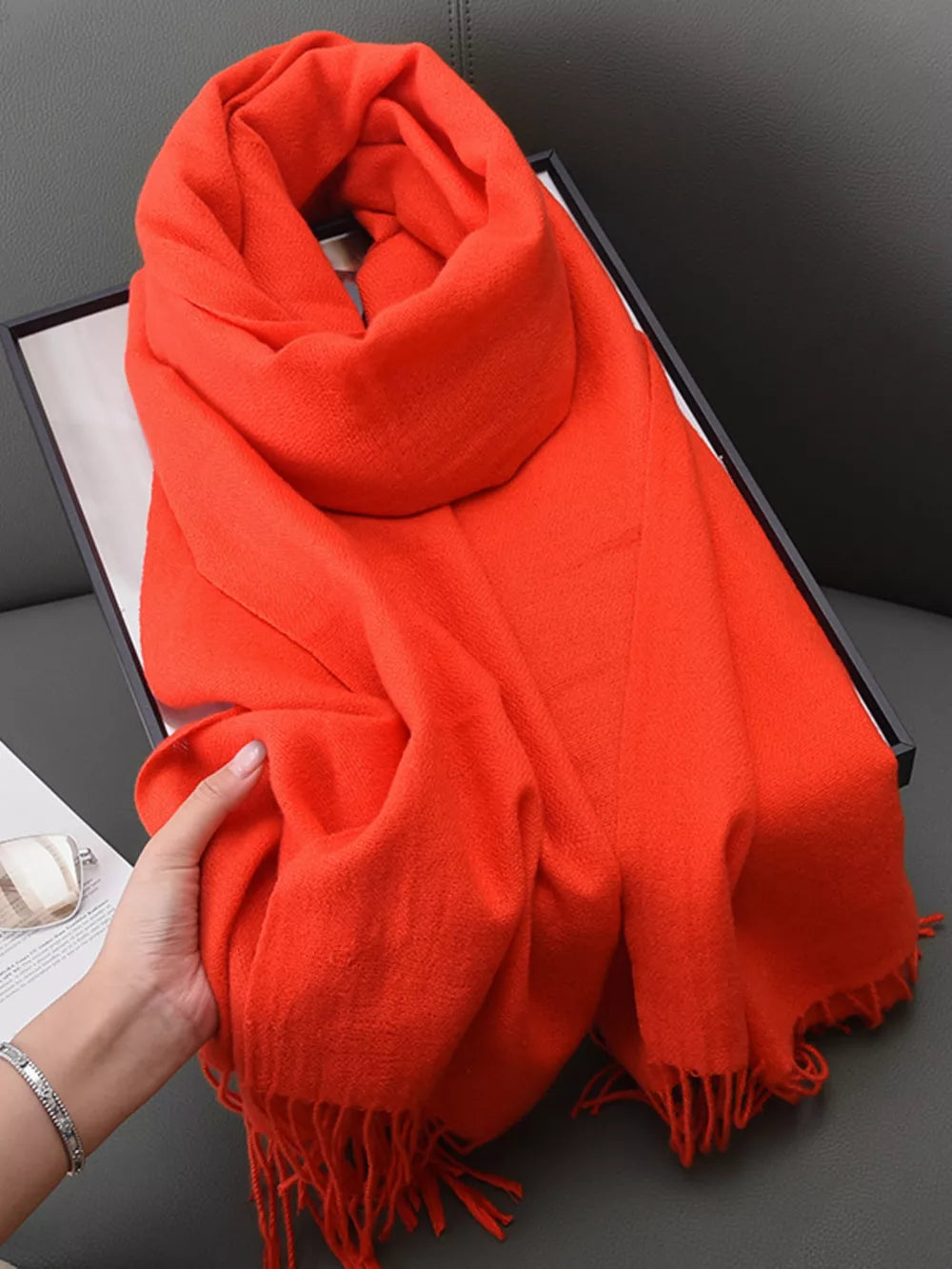 Orange scarf with fringe detail and a soft texture, styled in a box.