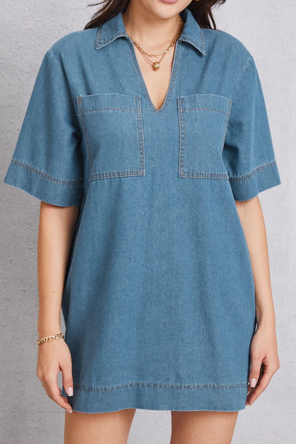 Denim mini dress with plunging collar, short sleeves, and chest pockets in medium wash.