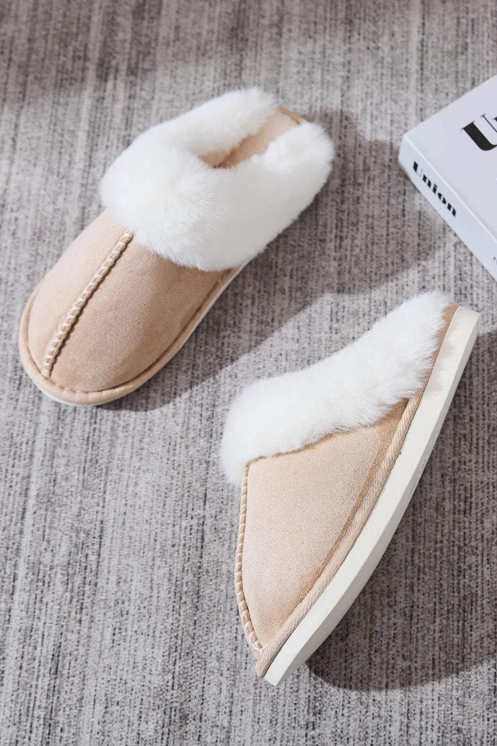 Beige suede house slides with white shearling trim and decorative stitching.