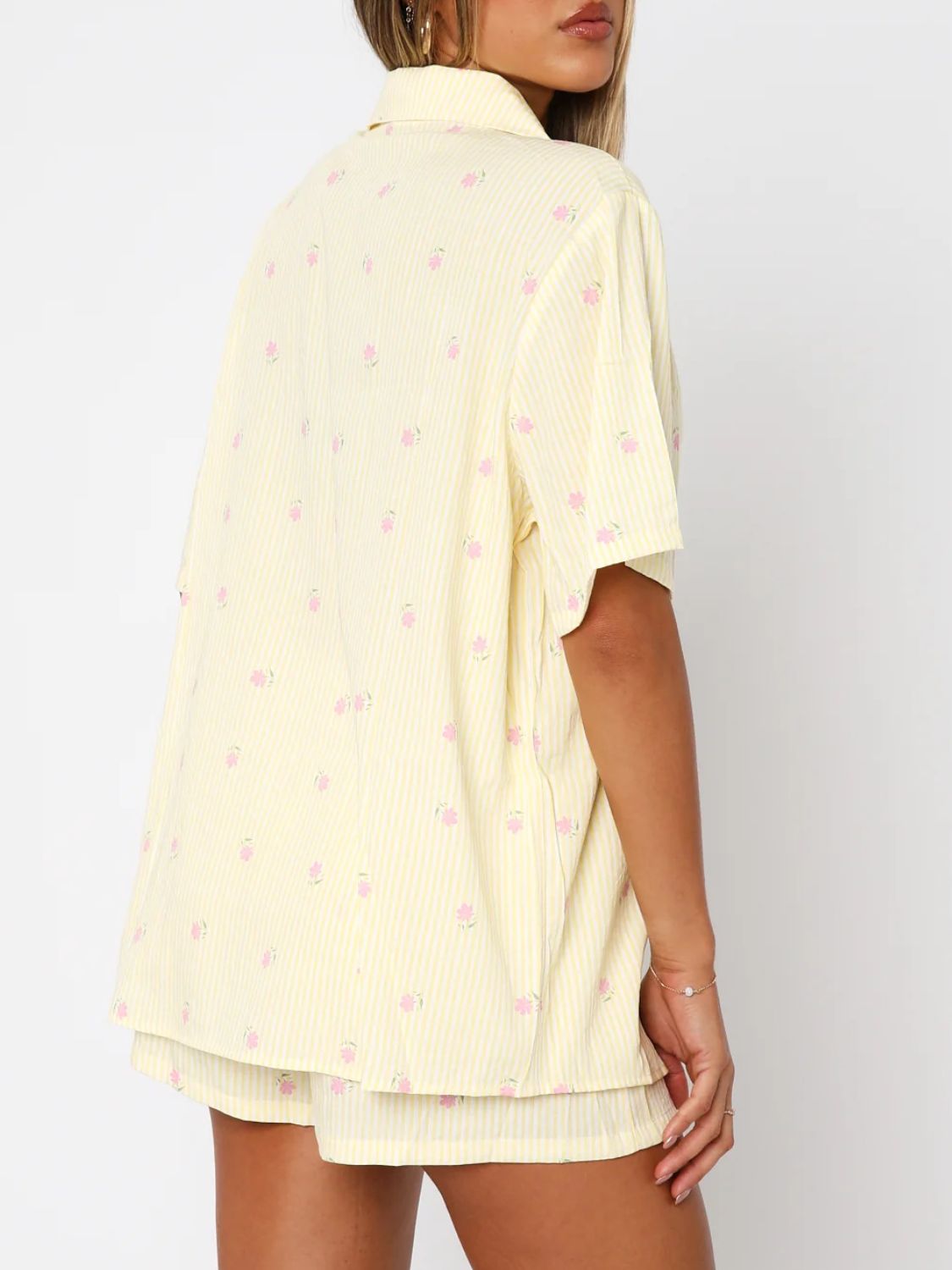 Pastel yellow striped pajama set with pink floral print, collared button-up top and shorts.