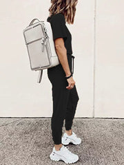Black casual round neck top and jogger pants set with drawstring waist, styled with white sneakers and a backpack.