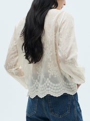 Sheer apricot long-sleeve blouse with floral embroidery and scalloped hem.