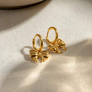 Gold hoop earrings with a detailed bow charm, 18K gold-plated.