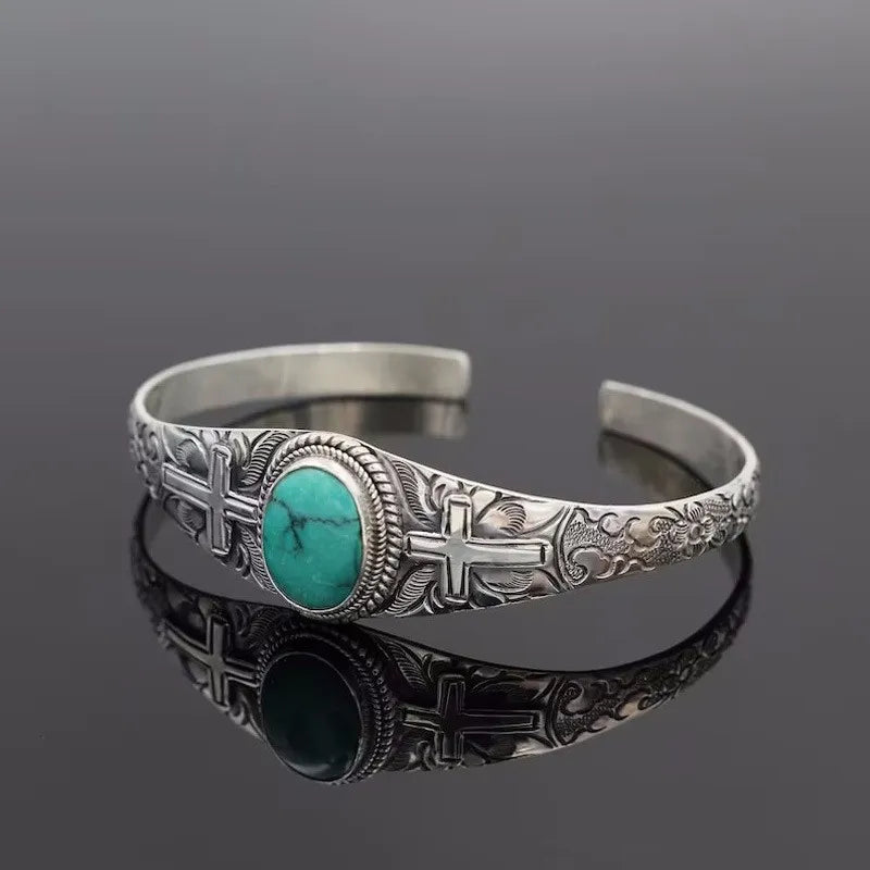 Turquoise cabochon open bangle with embossed crosses and floral details on silver-tone alloy.