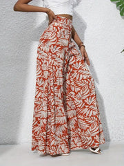 Orange-red palazzo trousers with a white tropical leaf print, made of 100% polyester.