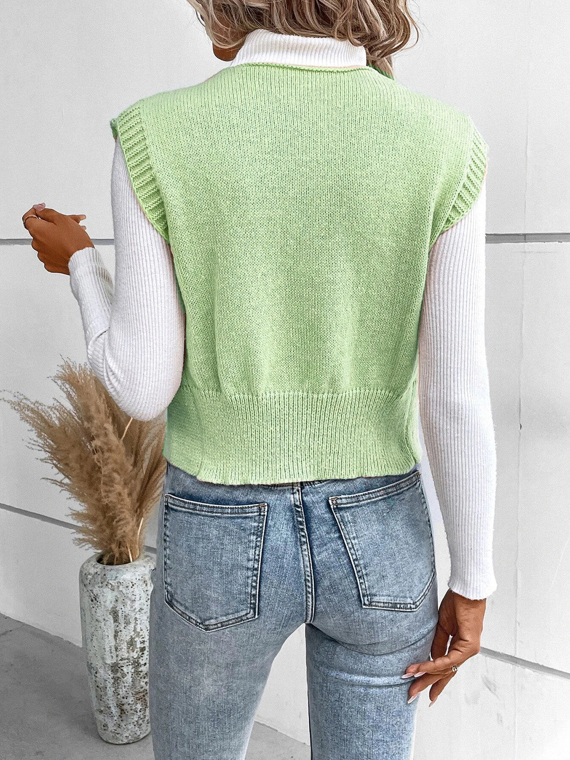 Light green knit vest with ribbed trim and a cropped hem, worn over a white turtleneck.