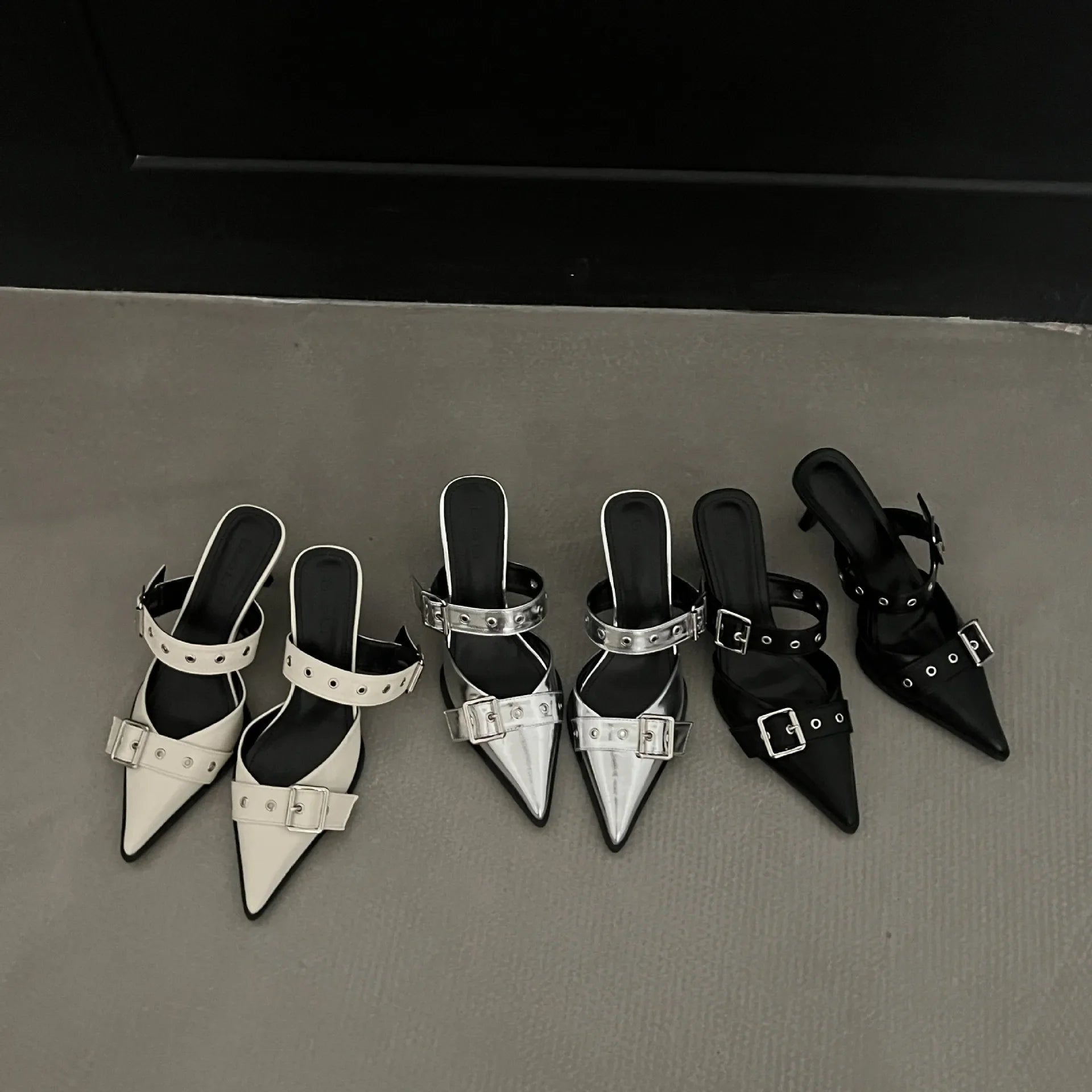 Metal pointed buckle mules in silver, beige, and black with strap details.