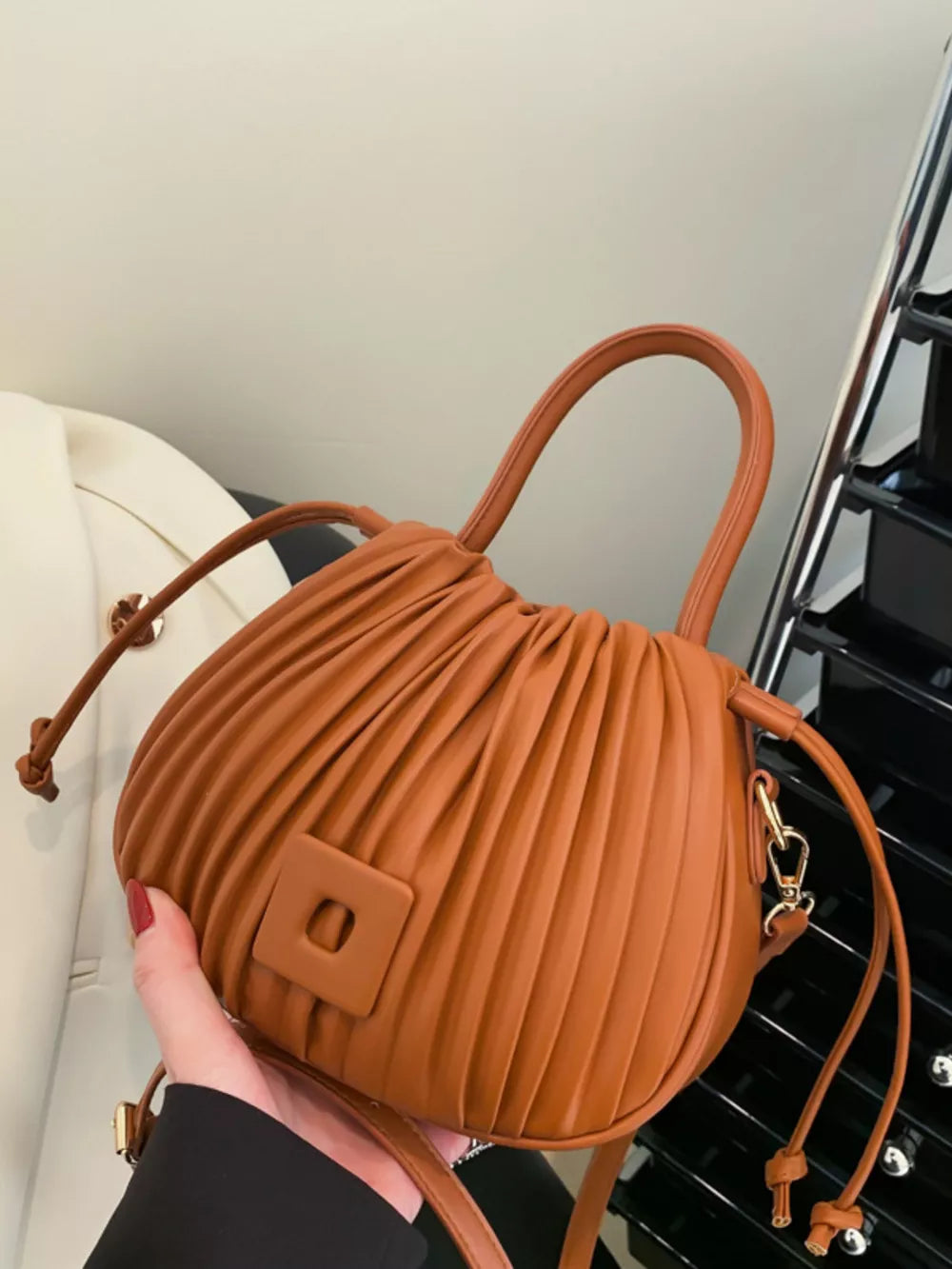 Brown pleated bucket bag with drawstring closure and square detail.