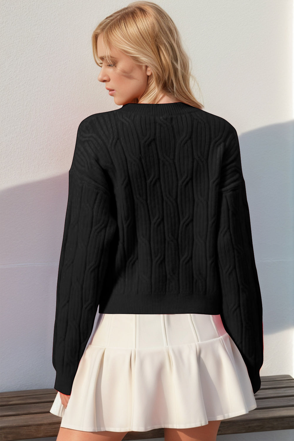 Black cable knit sweater with crew neck and long sleeves, styled with a white skirt.