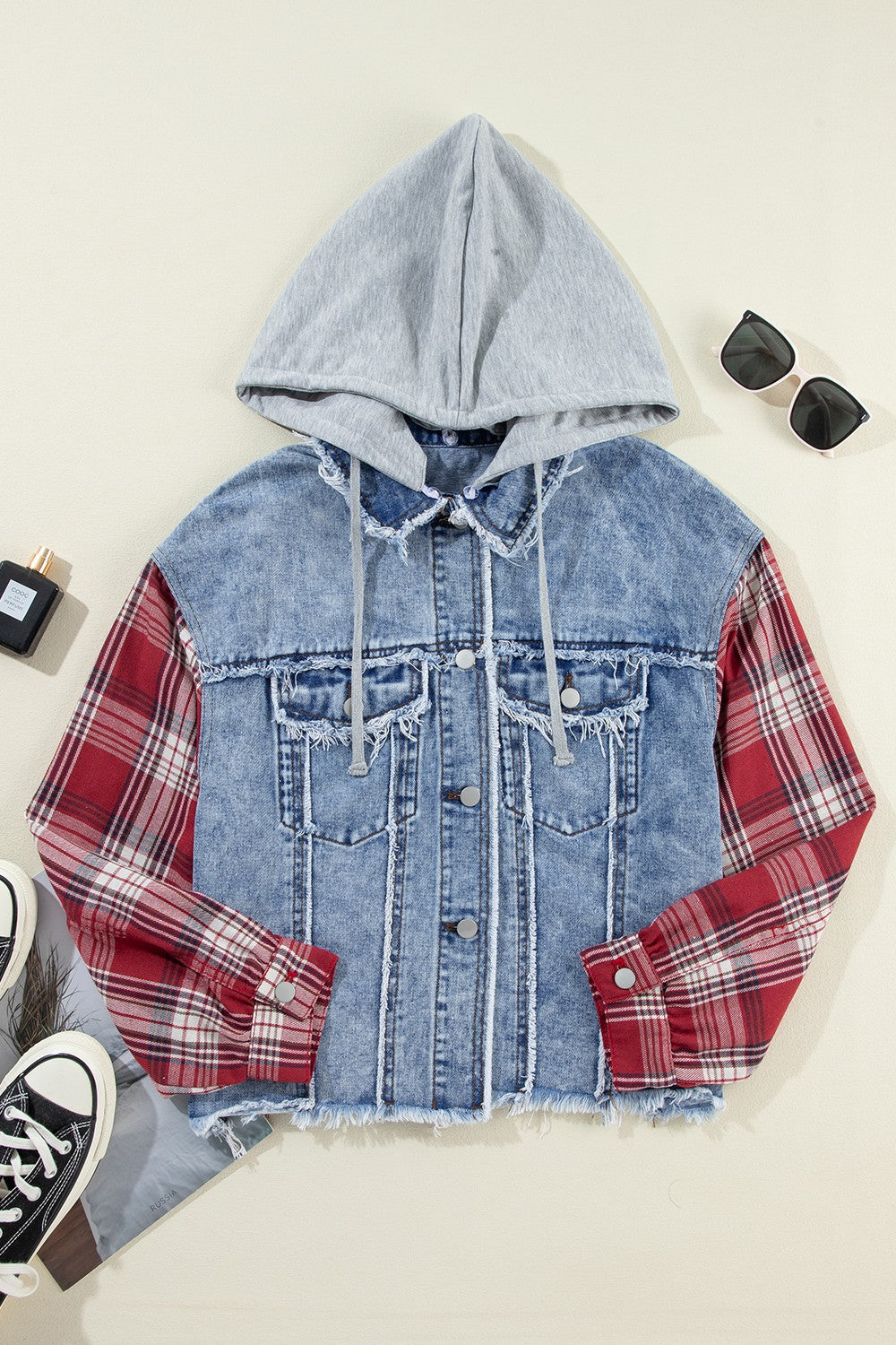 Denim trucker jacket with grey hood and red plaid sleeves, distressed details.