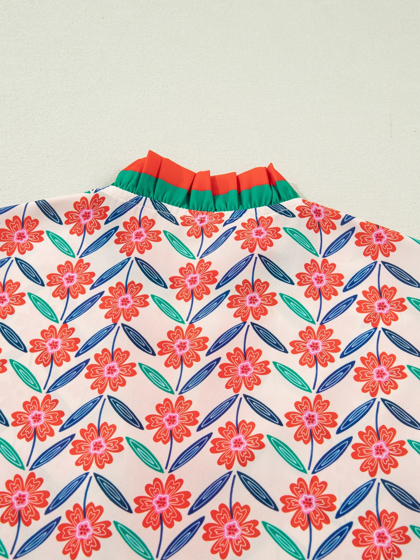 Floral ruffled v-neck shirt with orange and green striped trim and a colorful floral pattern.