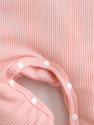 Blush pink waffle knit baby one-piece with white snap closures.