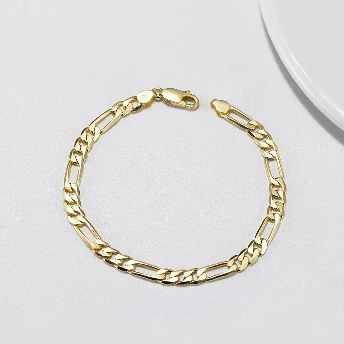Gold Figaro chain bracelet in sterling silver with alternating links and lobster clasp.