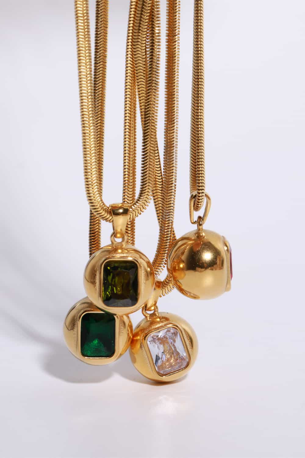 Gold snake chain necklaces with orb pendants featuring square cut gemstones in dark green, olive, and transparent.