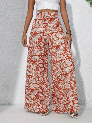 Orange-red palazzo trousers with a white tropical leaf print, made of 100% polyester.