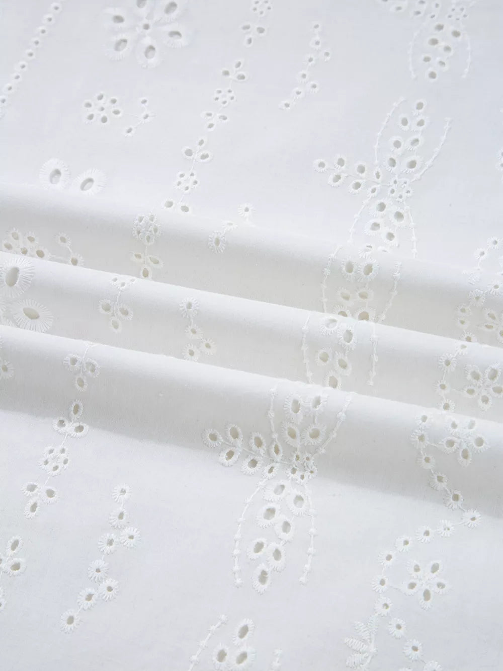 White cotton blouse with delicate eyelet embroidery and ruffled details.