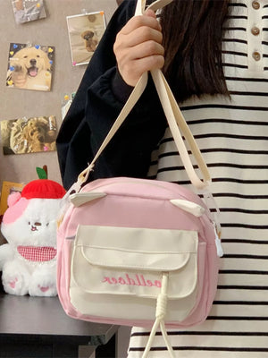 Pink crossbody bag with cat ears and dual front pockets, adjustable strap.