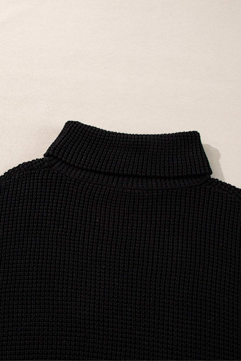 Black acrylic knit turtleneck sweater with ribbed texture and folded collar.