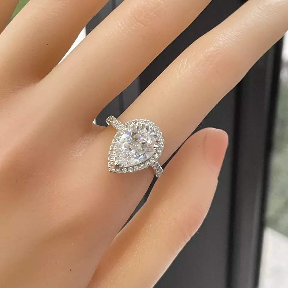Elegant moissanite teardrop ring in sterling silver with halo setting.