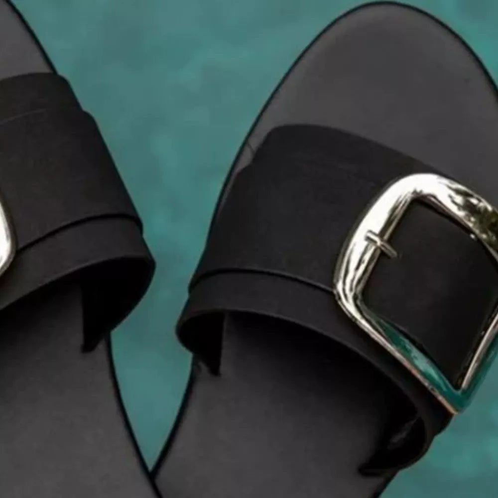 Black slide sandals with open toe and large silver buckle detail