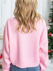 Pink acrylic knit sweater with ribbed texture and embroidered "Merry & Bright" detail.