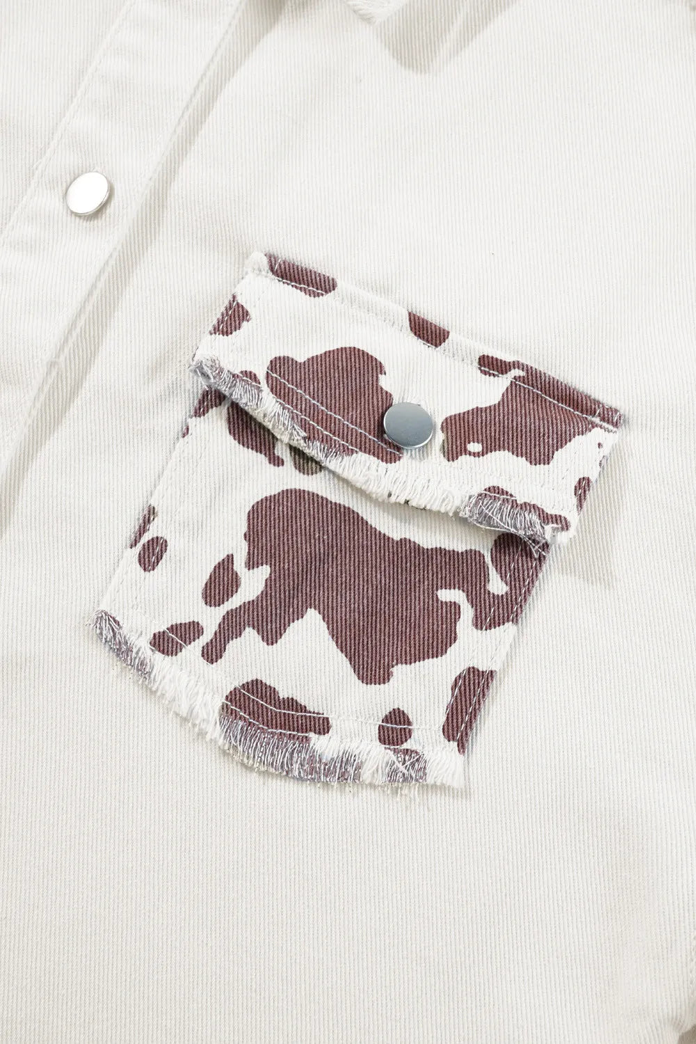 White cow print denim shacket with frayed pocket edges and silver snaps.