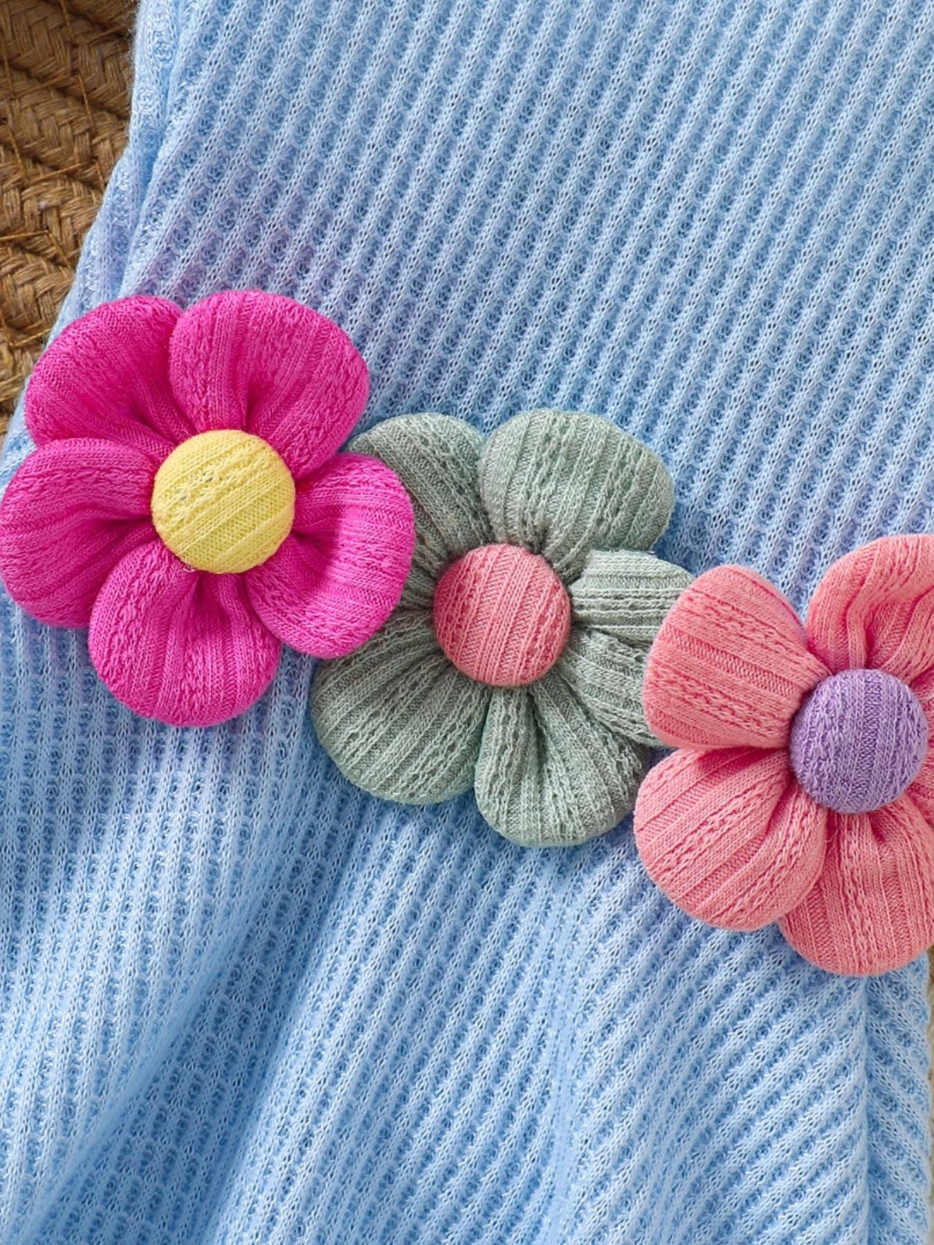 Baby jumpsuit in pastel blue waffle knit with floral appliques in pink, green, and coral.