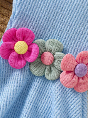 Baby jumpsuit in pastel blue waffle knit with floral appliques in pink, green, and coral.